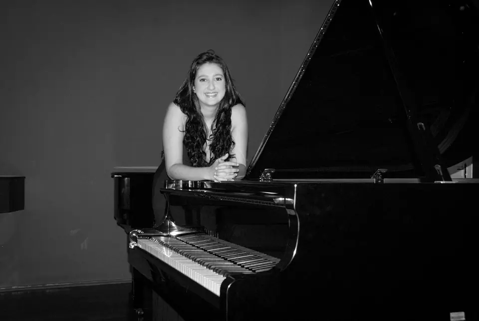 Raquel Gonçalves sorrindo, apoiada em um piano de cauda aberto, em preto e branco.