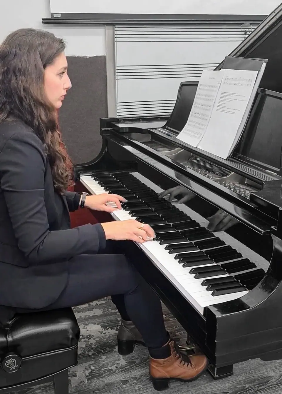 Raquel Gonçalves tocando um piano de cauda preto, de blazer escuro, em uma sala de paredes claras.